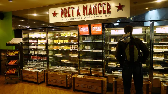 A Pret A Manger shop front inside a covered shopping centre, with its name in large letters above the entrance and a menu board beside the door.